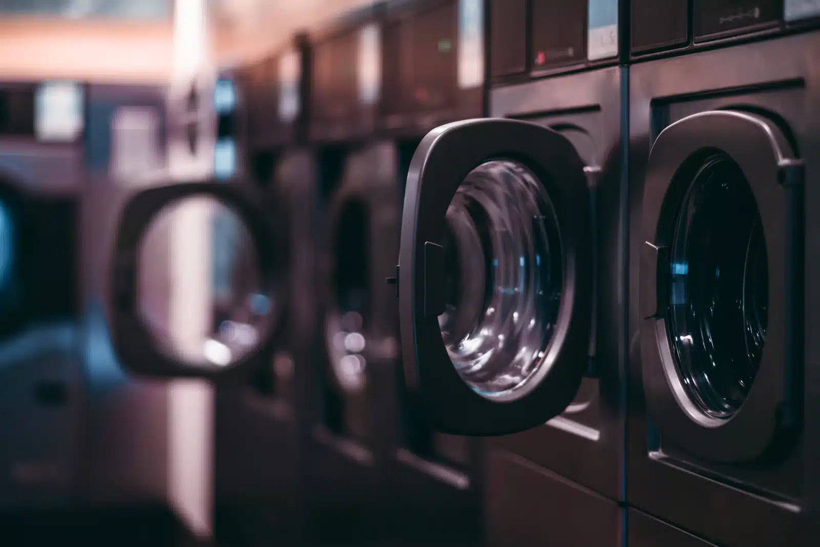 How On-Premise Laundry Systems Help Facilities Reduce Operational Costs | Coronet Equipment Row of commercial front-loading washing machines in a laundromat, with several machine doors open and ready for use.