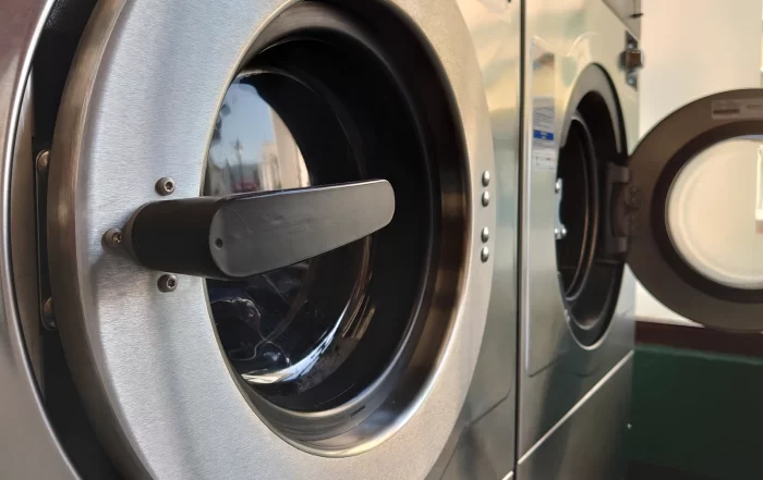 Close-up of commercial front-loading laundry machines with stainless steel doors, including one machine open and ready for use.