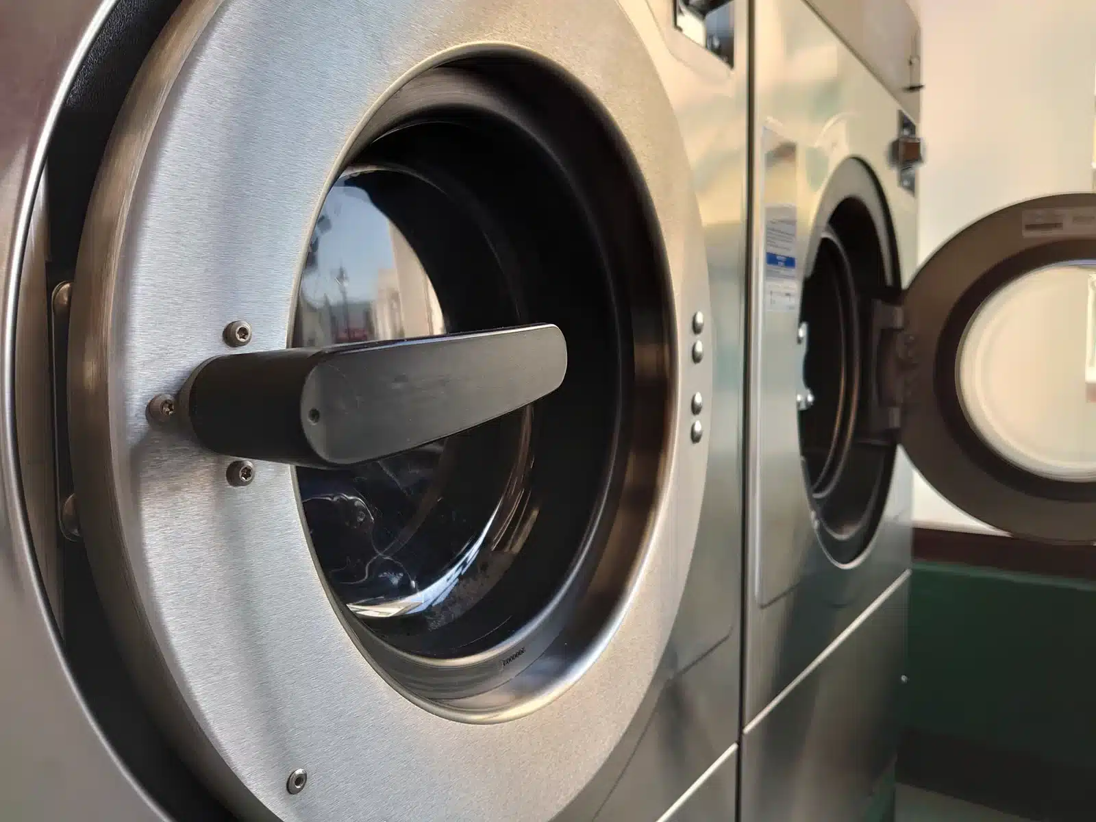 Close-up of commercial front-loading laundry machines with stainless steel doors, including one machine open and ready for use.