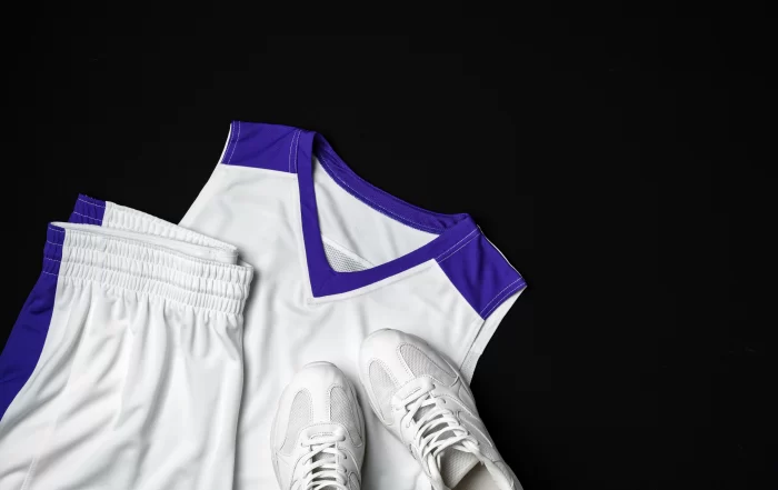 White and purple athletic basketball uniform with matching shorts and white sneakers displayed on a black background.