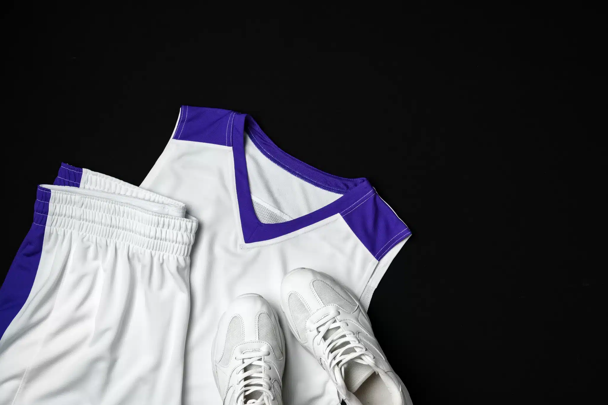 How Sports Laundry Systems Support Athletic Facilities and Teams | Coronet Equipment White and purple athletic basketball uniform with matching shorts and white sneakers displayed on a black background.