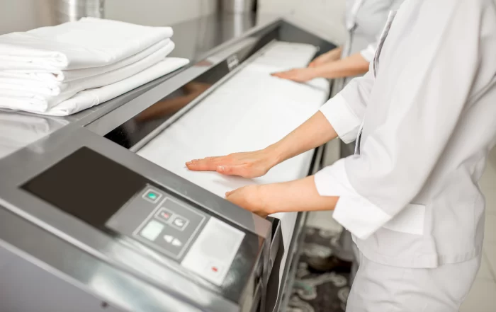 Laundry staff operating a commercial flatwork ironer to press and finish clean linens in an on-premise laundry facility.